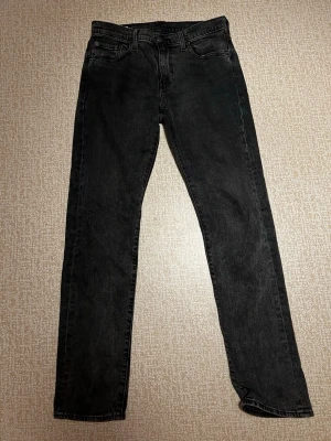 Svarta raka jeans från Levi's - Säljer ett par klassiska svarta jeans från Levi's med rak passform och fem fickor. Jeansen har en diskret tvättad look och är tillverkade i slitstark denim. Perfekta till en avslappnad stil och passar till det mesta. Storlek W30 L34. Priset kan diskuteras. Hör av dig vid absolut minsta fråga! 