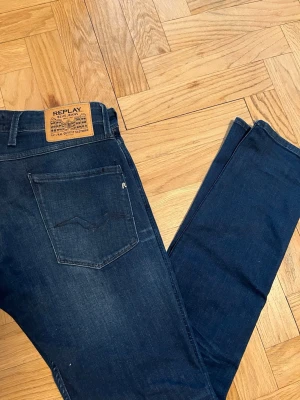 Mörkblå slim fit jeans från Replay - Säljer ett par mörkblå slim fit jeans från Replay med klassisk femficksdesign och snygga slitningar. Jeansen har en skön stretch och sitter tajt längs benen. Märkespatch bak i midjan och diskret logga på bakfickan. Storlek 31/34