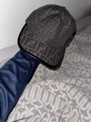 Svart keps med Fendi-logga helt ny endast 500 kr  - Säljer en svart keps från Fendi med det klassiska FF-monogrammet över hela kepsen. Kepsen har böjd skärm med svart kant och är tillverkad i ett tygmaterial som känns lyxigt och stilrent. Perfekt för dig som vill ha en statement-accessoar.