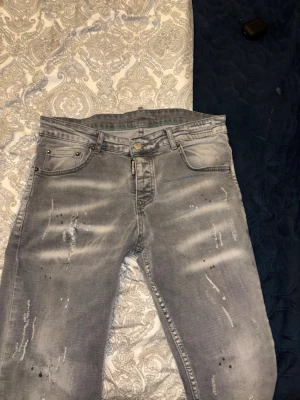 Grå slitna jeans från Dsquared2 - Säljer ett par grå jeans från Dsquared2 med slitningar och distressed detaljer framtill. Jeansen har klassisk femficksmodell, knappgylf och cool tvättad look. Perfekta för dig som gillar streetwear och vill ha en unik stil.