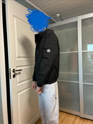 Svart vindjacka från Moncler - Snygg svart vindjacka från Moncler med dragkedja framtill och huva. Jackan har Moncler-logga på ärmen och en minimalistisk design. Tillverkad i ett lätt och vindtätt material, perfekt för blåsiga dagar. Passar dig som gillar stilrena och exklusiva plagg.