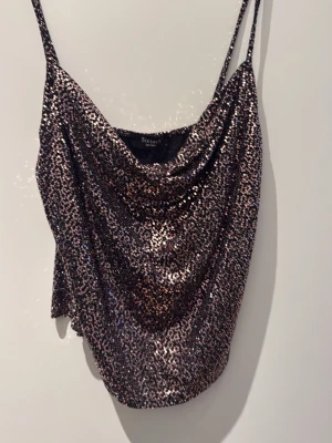 Glittrig paljettopp från Sisters Point - Säljer en glittrig topp från Sisters Point med tunna axelband och draperad front. Toppen är täckt av paljetter i silver och svart, perfekt för att sticka ut. Snygg croppad passform och passar till alla som vill glänsa lite extra.