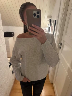 Ljusgrå off shoulder stickad tröja - Mysig ljusgrå stickad tröja med off shoulder-design och långa ärmar. Tröjan har en avslappnad passform och ribbstickade muddar vid ärmslut och nederkant. 