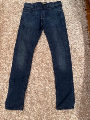 Mörkblå slim straight jeans från jack&jones  - Säljer ett par mörkblå Levi's jeans i klassisk straight modell med slim passform. Jeansen har fem fickor, normal midja och subtila slitningar framtill för en snygg vardagslook. Tillverkade i mjuk bomullsdenim med lite stretch för extra komfort.