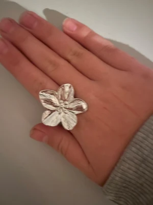 Chunky silvrig blomning  - Säljer en statementring i silverfärg med en stor, detaljerad blomma som motiv. Ringen har fem kronblad med fina räfflade detaljer som ger en cool och unik look. Perfekt för dig som vill sticka ut och addera något extra till din outfit.💗