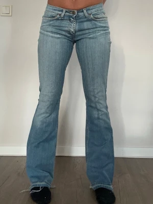 Ljusblå bootcut jeans - Säljer ett par ljusblå bootcut jeans med klassisk femficksmodell och låg midja. Jeansen har en lätt tvättad look och råa kanter vid bensluten för en avslappnad vibe. Perfekta till sneakers eller boots och ger en snygg siluett. RétroWear UF erbjuder special anpassning om du önskar extra hål i jeansen! Från 50kr. 