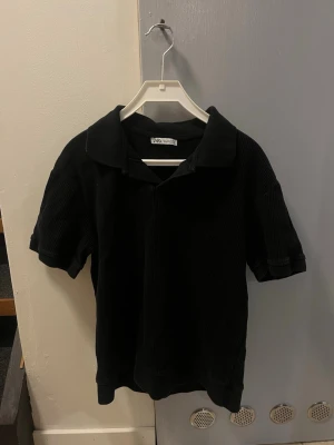 Svart manchester skjorta från Zara - Säljer en svart henley-skjorta från Zara i mjuk manchester. Skjortan har korta ärmar, klassisk krage och en relaxed fit. Knappt använt så är i perfekt skick