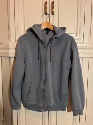 Grå zip hoodie från H&M Relaxed Fit - Säljer en ljusblå tröja från H&M i relaxed fit med dragkedja framtill, två fickor och justerbar huva med snören. Tillverkad i mjukt sweatshirtmaterial som är borstat på insidan för extra komfort. Pytteliten fläck på bröstet som säkert går att få bort
