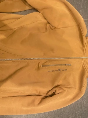 Brun vindjacka från Sail Racing XS - Snygg brun vindjacka från Sail Racing i storlek XS. Jackan har hel dragkedja framtill, en bröstficka med dragkedja och diskret logga på bröstet. Tillverkad i ett mjukt och slitstarkt material som passar perfekt till blåsiga dagar.