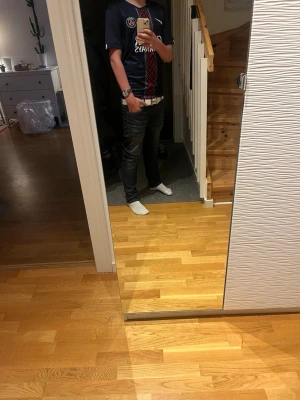 PSG matchtröja mörkblå herr - Säljer en mörkblå Paris Saint-Germain matchtröja från Nike med röda och vita detaljer samt klubbmärke och sponsortryck på bröstet. Tröjan har korta ärmar och sportig passform, perfekt för fotboll eller träning.