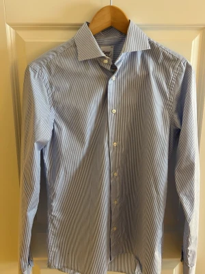 Blåvit randig skjorta från Oscar of sweden  - Klassisk blåvit randig skjorta med lång ärm och knappar framtill. Skjortan har en stilren krage och smala ränder för en clean look.