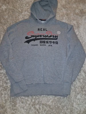 Superdry hoodie grå - Jag säljer en fin superdry hoodie som är i bra skick, hoodien är i storlek M och passar som en M, skriv gärna till mig vid minsta intresse, perfect nu till vintern😊