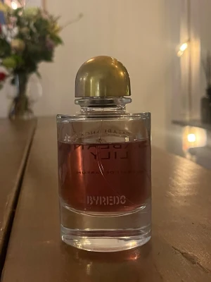 Byredo parfym med guldlock - Säljer en elegant parfym från Byredo med rund glasflaska och guldigt lock. Doften har en djup rosa färg och flaskan har Byredos logga tryckt framtill. Perfekt för dig som gillar lyxiga och stilrena parfymer.