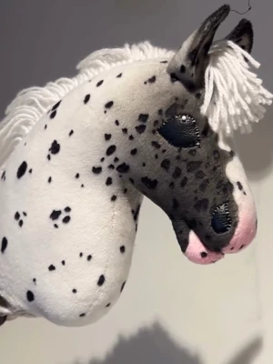 Prickig käpphäst med vit man - Unik käpphäst med vit botten och svarta prickar, sydd i mjukt tyg. Hästen har en fluffig man av vitt garn och detaljerad nos med rosa inslag. Perfekt för dig som gillar hästar och vill ha något personligt till leken.