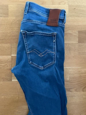Blå jeans från Replay Hyperflex - Snygga blå jeans från Replay Hyperflex med klassisk femficksmodell och kontrastsömmar. Jeansen har en skinnpatch bak i midjan och diskret Replay-logga vid fickan. Materialet är stretchigt för extra komfort och passform.