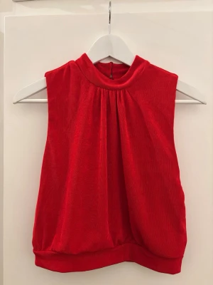 Röd ärmlös topp med öppen rygg - Snygg röd ärmlös topp med hög hals och fina veck framtill. 
