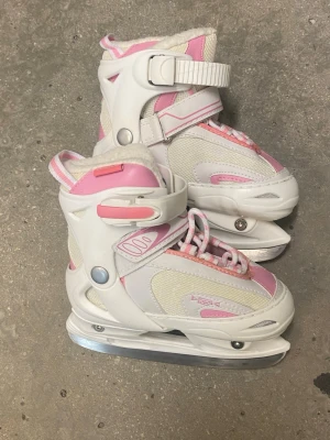 Vita och rosa skridskor med spänne strl 33 - Säljer ett par vita och rosa skridskor med justerbart spänne och snörning. Skridskorna har en robust plast- och textilkonstruktion, meshpaneler för ventilation och mjuk vaddering inuti för extra komfort. Perfekta för dig som vill ha snygga och funktionella skridskor på isen. Barnstorlek 33.