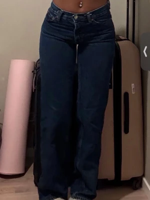 Mörkblåa raka jeans - Säljer ett par mörkblåa jeans med rak passform och låg midja. Jeansen har klassisk femficksdesign och stängs med knapp och dragkedja. Perfekta för en avslappnad och trendig look.