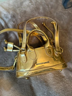 Väska  - Snygg miniguldväska med både handtag och axelband. Knappt använd.