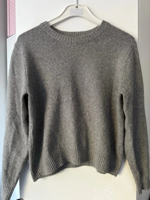 Grå stickad tröja från H&M - En enkel och stilren grå stickad tröja från H&M. Tröjan har rund halsringning, långa ärmar och ribbade muddar vid hals, ärmslut och nederkant. Perfekt basplagg i garderoben och passar till det mesta. Fin men lite nopprig..