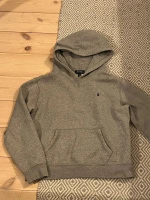 Grå hoodie från Polo Ralph Lauren - Säljer en stilren grå hoodie från Polo Ralph Lauren med en broderad logga på bröstet och mjukt material som känns skönt mot huden. Perfekt för en avslappnad Grisch stil. Mycket bra skick kontakta om intresse!