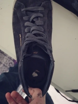 Mörkblå sneakers från Jim Rickey - Snygga mörkblå sneakers från Jim Rickey i mocka med klassisk låg profil och vita sulor. Skorna har matchande mörkblå skosnören och diskret logga i guld på sidan. Perfekta för dig som gillar stilrena och tidlösa sneakers i schysst material.