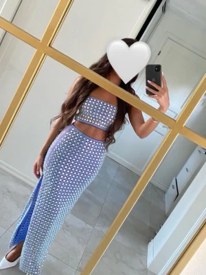 Blå glittrig långklänning med slits från OH POLLY - Säljer en blå långklänning med glittriga paljetter och öppen midja. Klänningen har en slits på sidan och är ärmlös med bandeau-topp. Perfekt för dig som vill sticka ut på festen! Den är från oh polly och även tagits till skräddaren och gjort toppen lite längre än vad originalet var!