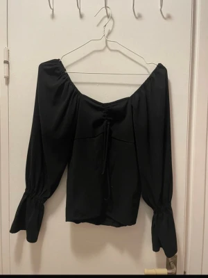 Svart topp -  svart topp. Kan bäras som på bilden eller offshoulder. med långa puffärmar och snörning framtill. resår vid ärmsluten för extra volym. Anvönd men i bra skick!! Från pieces, men har klippt bort lappen :) Skulle säga att den passar S-M