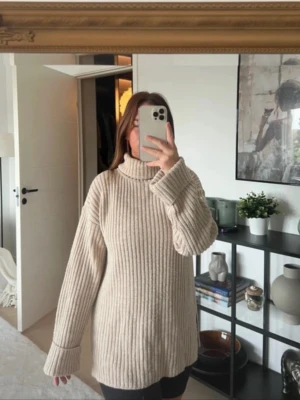 Beige stickad polotröja - Mysig beige stickad polotröja med breda ribbade ränder och långa ärmar. Tröjan har en avslappnad, oversized passform och hög krage som ger extra värme. Perfekt för lager-på-lager och en chill look.