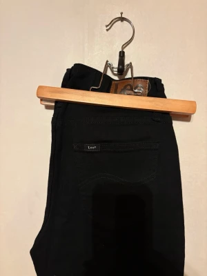 Svarta  bootcutjeans från Lee - Säljer ett par svarta jeans från Lee med bootcut passform. Jeansen har fem fickor, Lee-logga på bakfickan och läderpatch i midjan. Perfekta till en avslappnad stil och tillverkade i slitstarkt denimtyg. W25/L31