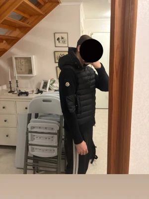 Moncler Cardigan  - Säljer en svart dunjacka från Moncler med huva och dragkedja framtill. Jackan har Moncler-logga på ärmen och är tillverkad i glansigt material på framsidan och ärmar i mjukare tyg. Perfekt för kalla vinterdagar och riktigt snygg streetstil.