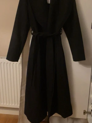 Svart lång kappa med knytskärp - Helt ny lång kappa från Ellos. Endast testad innan🤗I storlek xs i färgen svart. Lapp sitter kvar, se bild. Ny pris 799kr. Hör av er vid frågor🌸