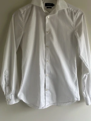 Vit skjorta från Riley (Super Slim Fit) - Klassisk vit skjorta från Riley i super slim fit-modell. Skjortan har lång ärm, knappar framtill och en stilren krage. Perfekt för dig som gillar en smalare passform och enkel, clean stil. Tillverkad i bomull för en bekväm känsla.