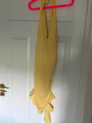 Gul långklänning med volang - Snygg gul långklänning med breda axelband och volangdetaljer nedtill. Klänningen har en elegant och figurnära passform som ger en stilren look. Perfekt för sommarens alla tillfällen när du vill sticka ut lite extra.