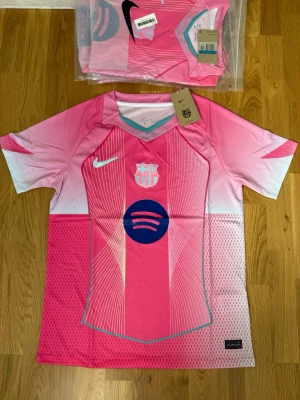 Barça x Nike rosa matchtröja - Snygg rosa FC Barcelona matchtröja från Nike med vita och ljusblå detaljer. Tröjan har klubbmärke, Nike-logga och Spotify-logga på bröstet. Tillverkad i lätt och ventilerande polyester, perfekt för fotboll eller träning.