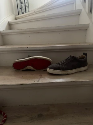Gråa Christian Louboutin sneakers - Snygga gråa sneakers i mocka från Christian Louboutin med klassisk röd sula. Skorna har lågt skaft, rund tå och matchande gråa skosnören. Perfekta för dig som vill ha en stilren och exklusiv look. Jag kommer göra dom mer rena om någon vill köpa dom