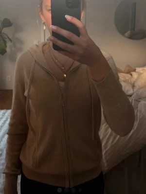 Beige hoodie med dragkedja - Mysig beige hoodie med dragkedja framtill och huva. Tillverkad i ett mjukt, stickat material som känns skönt mot huden. Perfekt för en avslappnad look och enkel att matcha med olika outfits. Klassisk passform och ribbade muddar vid ärmslut och nederkant. Den har ett hål som går att laga om man lämnar in den därav priset. Pris kan diskuteras och tryck inte på köp nu