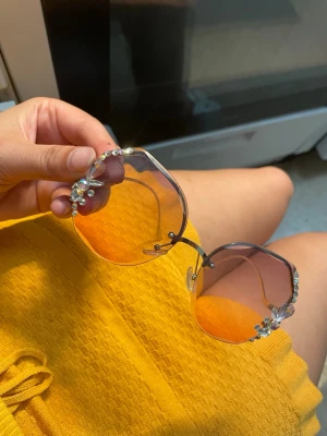 Rosa solglasögon med stenar - Unika solglasögon med stora, oktagonformade rosa glas och tunna guldfärgade bågar. Utsmyckade med glittrande stenar och pärlor i hörnen för en extra cool och trendig look. Perfekta för dig som vill sticka ut i sommar!