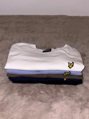Fyrpack Lyle & Scott t-shirts - Säljer fyra stilrena t-shirts från Lyle & Scott i vitt, ljusblått, brunt och marinblått. Alla har klassisk passform, korta ärmar och den ikoniska gula loggan broderad på bröstet. 