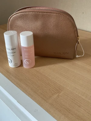 Thalion necessär med hudvårdsprodukter - Säljer en snygg necessär i skimrande beige/roséguld från Thalion, tillsammans med två miniflaskor: en ansiktsrengöring och ett ansiktsvatten. Perfekt för resan eller gymväskan. Båda flaskorna är 35 ml och har praktiska vita lock.