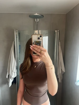 Brun ärmlös topp i stretchigt material - Säljer en brun, tight och ärmlös topp med hög hals. Toppen är gjord i ett stretchigt och mjukt material som sitter snyggt mot kroppen. 