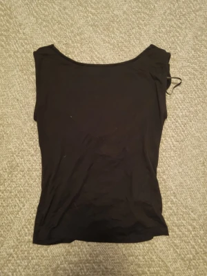 Svart ärmlös topp med drapering - Säljer en svart, ärmlös topp med snygg draperingl. Toppen har en enkel, stilren design och är tillverkad i ett mjukt och stretchigt material som sitter bekvämt mot kroppen. Perfekt att matcha med jeans eller kjol.