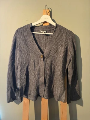 Grå ribbad kofta från Object - Mysig grå kofta från Object i ribbstickat material. Koftan har v-ringning, långa ärmar och knäppning framtill med en knapp i trälook. Priset går att prata om. Perfekt att slänga över en t-shirt eller linne för en avslappnad stil.