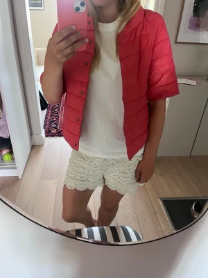 Rosa quiltad dunväst - Säljer en rosa quiltad dunväst med tryckknappar framtill och korta ärmar. Vänster fickas knapp har lossnat