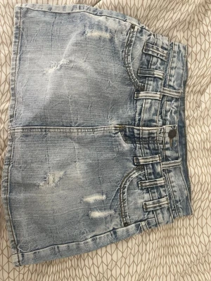 Ljusblå jeanskjol med slitningar - Säljer en oanvänd ljusblå jeanskjol med slitna detaljer och klassiska fickor både fram och bak.