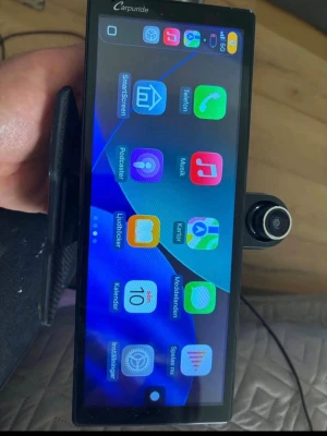 Carpuride CarPlay skärm med kamera - Stor svart Carpuride CarPlay skärm med touchfunktion och flera appar, perfekt för bilen. Inkluderar kamera, fäste, laddkabel och manual. Skärmen har modern design med rundade hörn och tydliga ikoner. Passar för navigation, musik och samtal.
