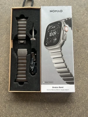 Nomad Stratos Band Apple Watch titan - Nomad Stratos Band är ett armband i naturlig titan för Apple Watch 45mm, 46mm och 49mm. Bandet har en stilren, silverfärgad länkdesign och levereras med verktyg för enkel justering. Perfekt för dig som vill ha en exklusiv och modern känsla på din klocka. Man får med extra länkar