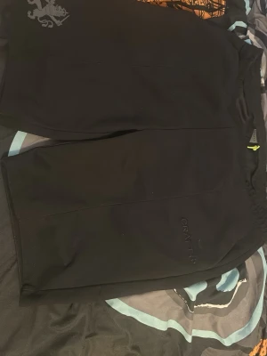 Svarta träningsshorts från Craft - Svarta träningsshorts från Craft med diskret logga på benet och elastisk midja med gul snörning. Tillverkade i ett lätt och funktionellt syntetmaterial som passar perfekt för sport och aktivitet.