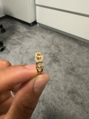 Guldring i kedjemönster från GHA - Snygg guldring från GHA i 18K guld med ett trendigt kedjemönster. Ringen har en öppen design med detaljerade länkar som ger en cool och modern känsla. Perfekt för dig som vill ha något unikt och stilrent i din smyckessamling.