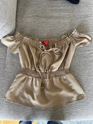 offshoulder topp från Guess - Snygg beige offshoulder topp från Guess med smock i midjan och axlarna. Storlek S